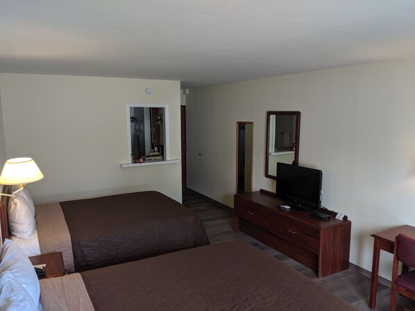 Habitación de hotel con dos camas, un escritorio con televisor, un aparador y una lámpara.