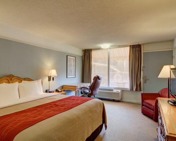 A hotel room with a large bed, a desk, a chair, and a window with blinds.