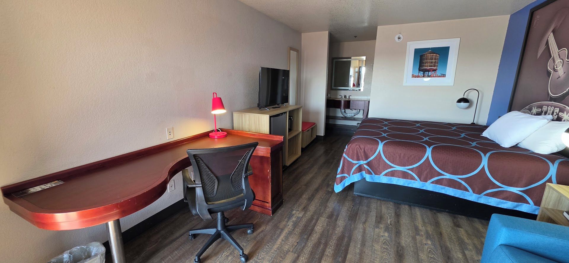 A hotel room with a desk, chair, bed, and a television.