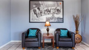 A room with two leather sofas, a small table with a lamp, a framed welcome sign, and a vase with dried plants. - Super 8 by Wyndham Cleburne (Cleburne)
