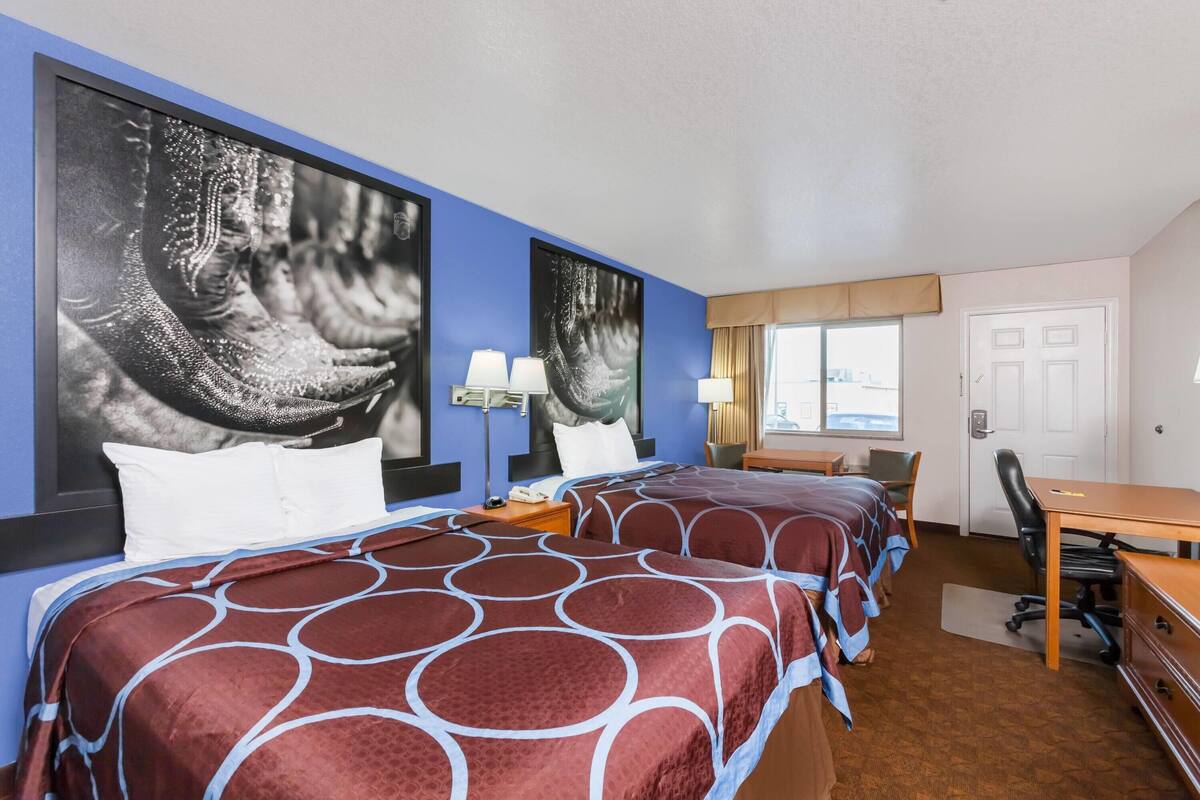 A hotel room with two beds, a desk, a chair, a lamp, and a window.