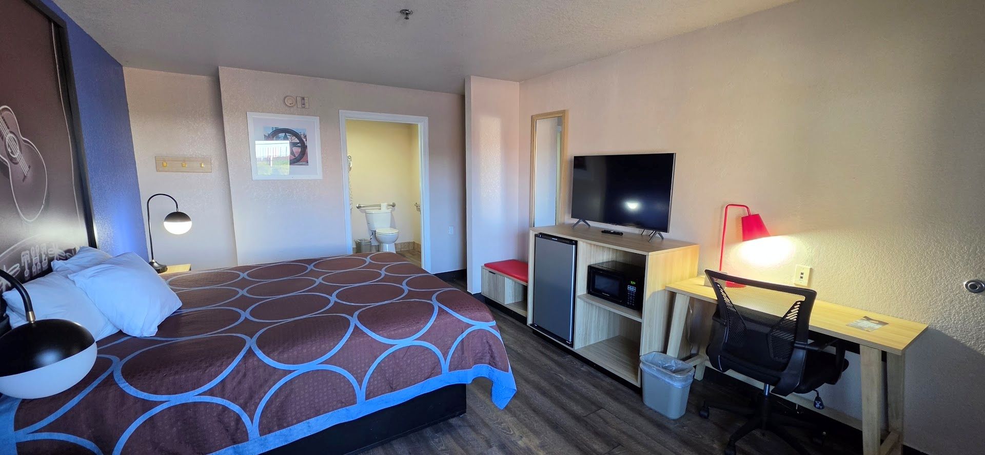 Een hotelkamer met een bed, een bureau met een computer, een televisie en een prullenbak.