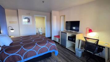 A hotel room with a bed, a desk with a computer, a television, and a trash bin.