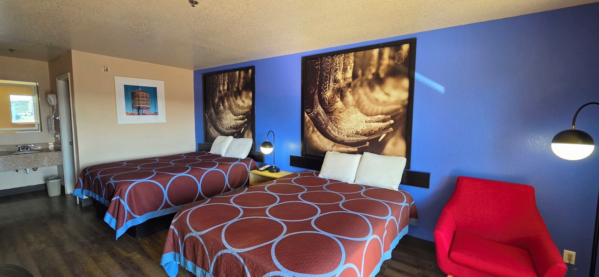 A hotel room with two beds, a red chair, and artwork on the walls.