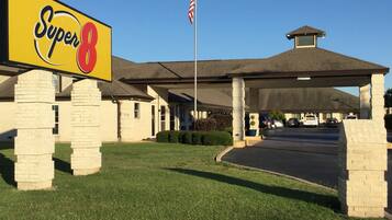 Un hotel Super 8 con un letrero grande, una zona de estacionamiento techada y una bandera.