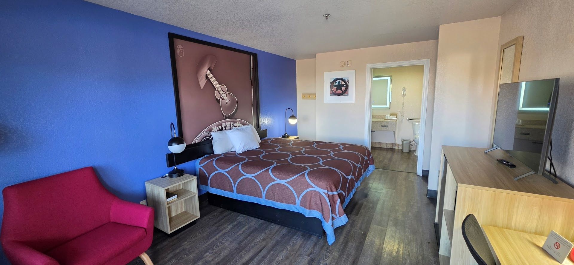 A hotel room with a bed, a desk, a chair, and a television.