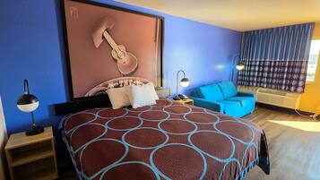 A hotel room with a bed, a blue sofa, a guitar decoration, a lamp, and a window with curtains.
