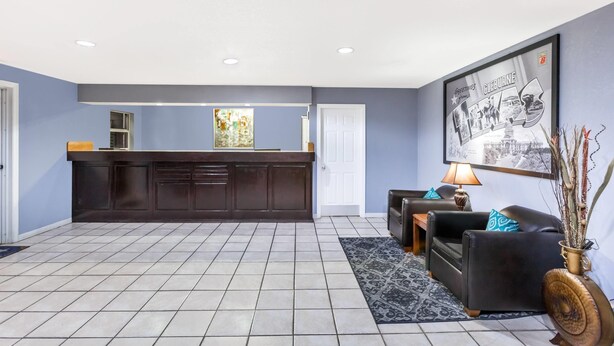 A spacious room with a dark wooden reception desk, a black leather sofa, a patterned rug, and a framed picture on the wall. - Super 8 by Wyndham Cleburne (Cleburne)