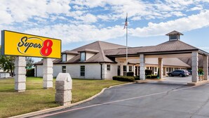 A Super 8 hotel with a covered parking area, a flagpole with an American flag, and a clear sky. - Super 8 by Wyndham Cleburne (Cleburne)