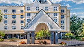 Ein Fairfield by Marriott Inn & Suites Gebäude mit markantem Eingangsbogen, zahlreichen Fenstern und einer begrünten Vorderseite mit Palmen.