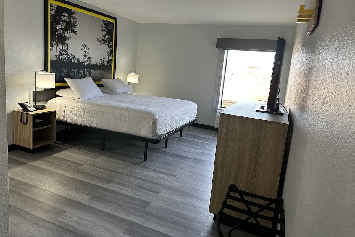 Una habitación de hotel con cama, lámparas de noche, escritorio y un ventanal grande.