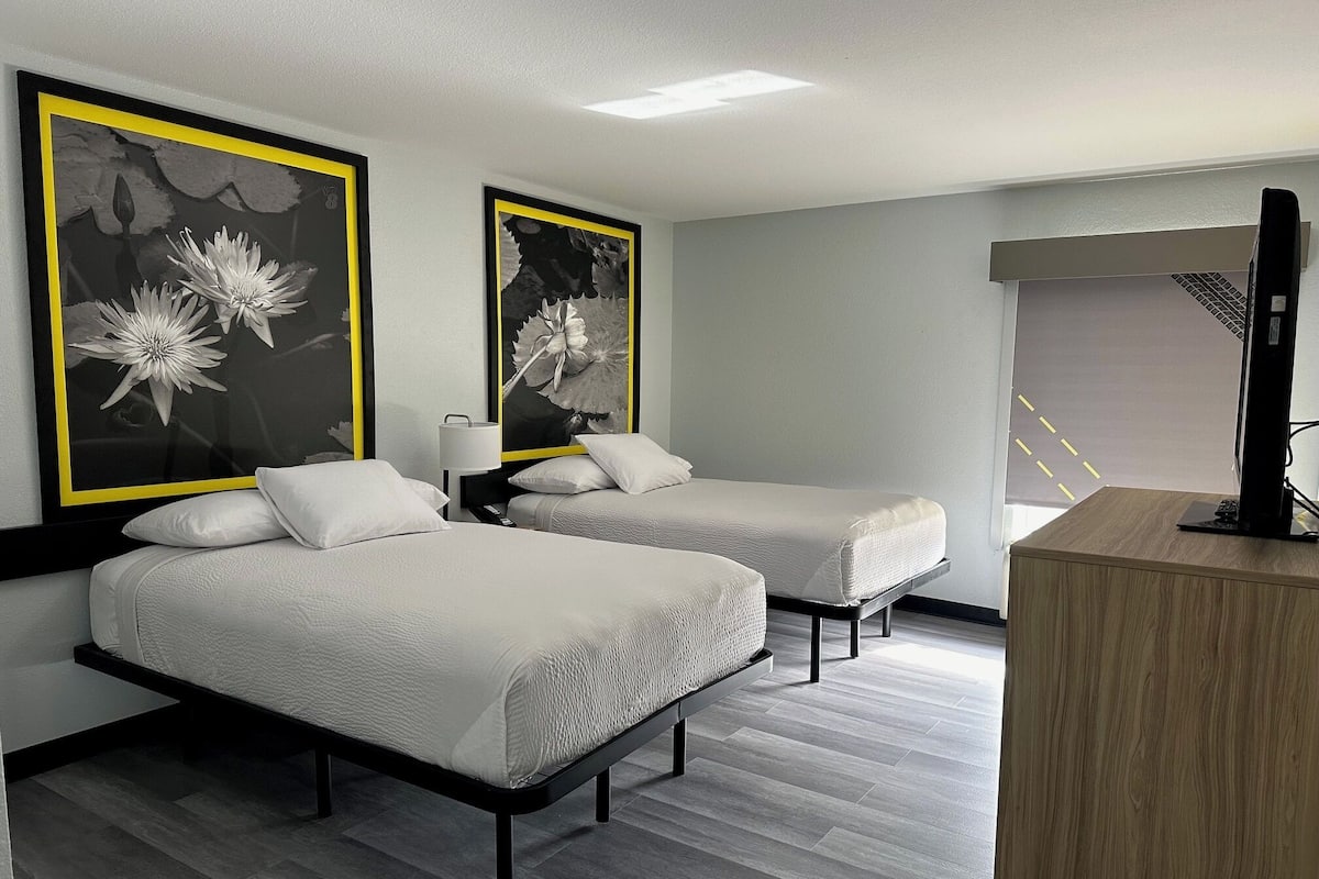 Habitación de hotel con dos camas, un escritorio y obras de arte en las paredes.