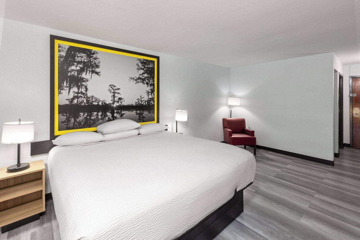 Habitación de hotel moderna con una cama grande, dos lámparas de noche, una silla roja y una obra de arte colgada en la pared.