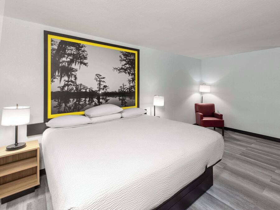 A modern hotel room with a large bed, two bedside lamps, a red chair, and a wall-mounted artwork.