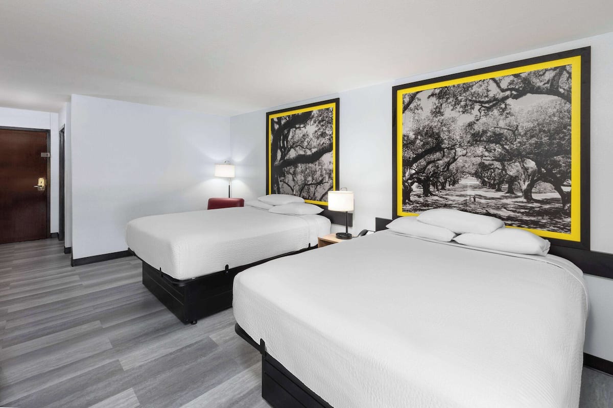Habitación de hotel con dos camas, una mesita de noche con lámparas y fotografías en blanco y negro de árboles en las paredes.