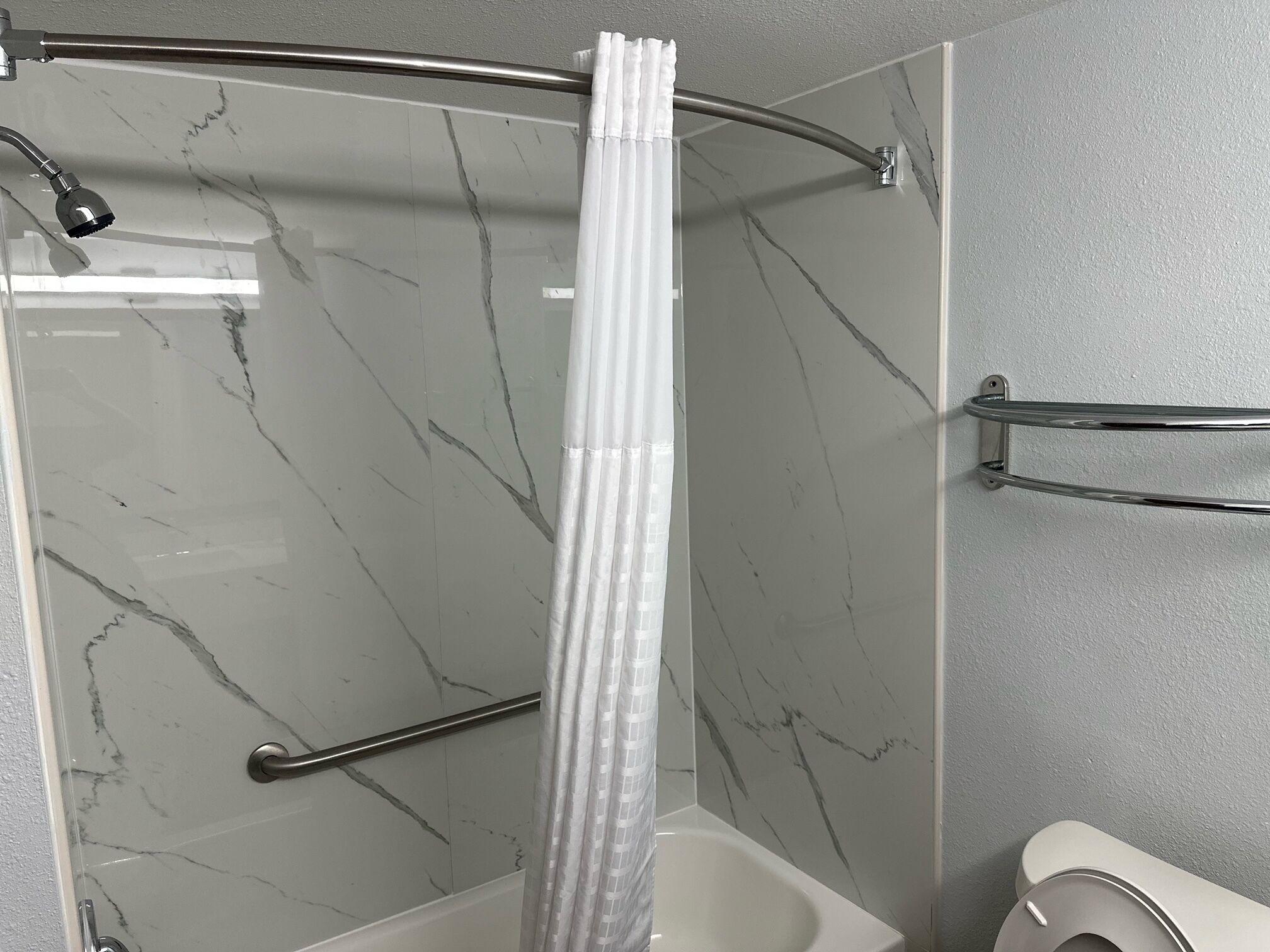 A shower area with a curved glass door, a handheld showerhead, a grab bar, and a towel rack.