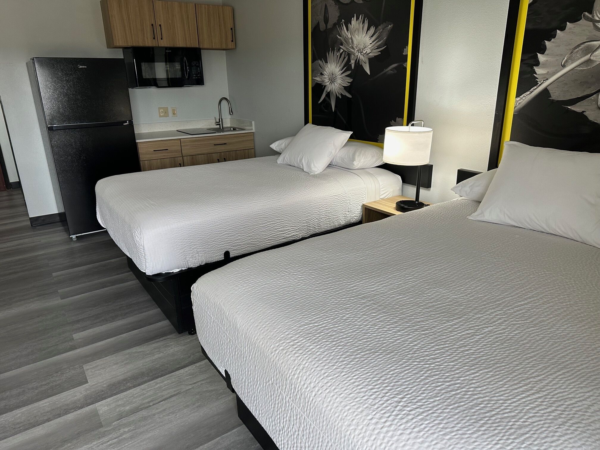Une chambre d’hôtel avec deux lits, une kitchenette et un téléviseur fixé au mur.