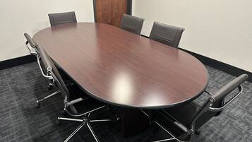 Una mesa de conferencias con cuatro sillas, una puerta y piso alfombrado.