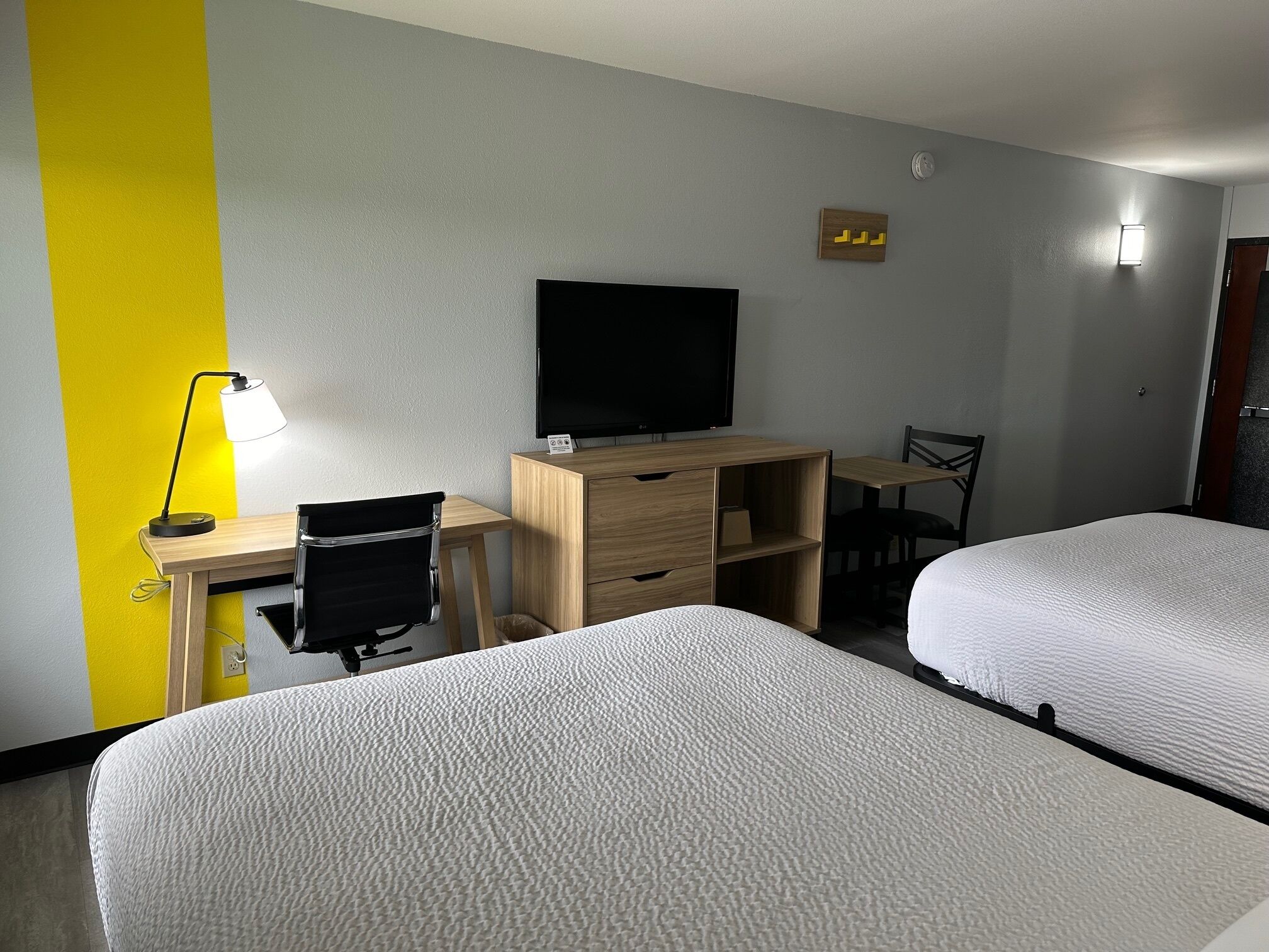 A hotel room with two beds, a desk with a chair, a television, and a lamp.