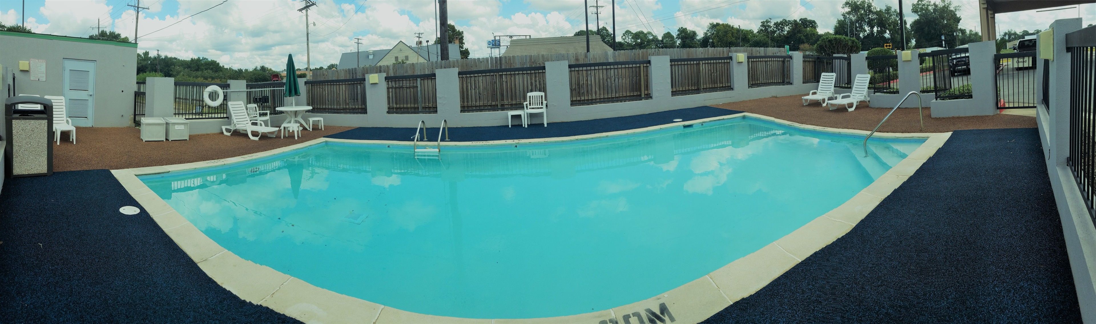 Una piscina con borde azul, rodeada por una cerca y sillas de descanso.