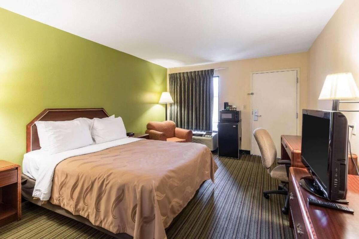 Ein Hotelzimmer mit einem Bett, einem Schreibtisch mit Computer, einem Fernseher und einem Sessel.