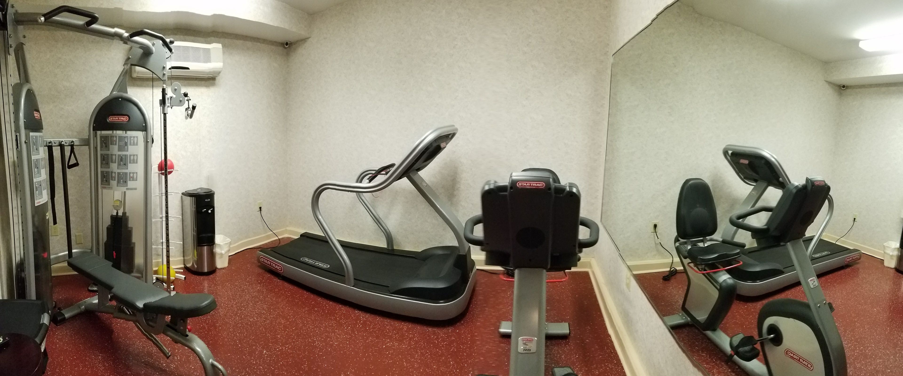 Un gimnasio con máquinas de cardio, equipo de levantamiento de pesas y un espejo grande.
