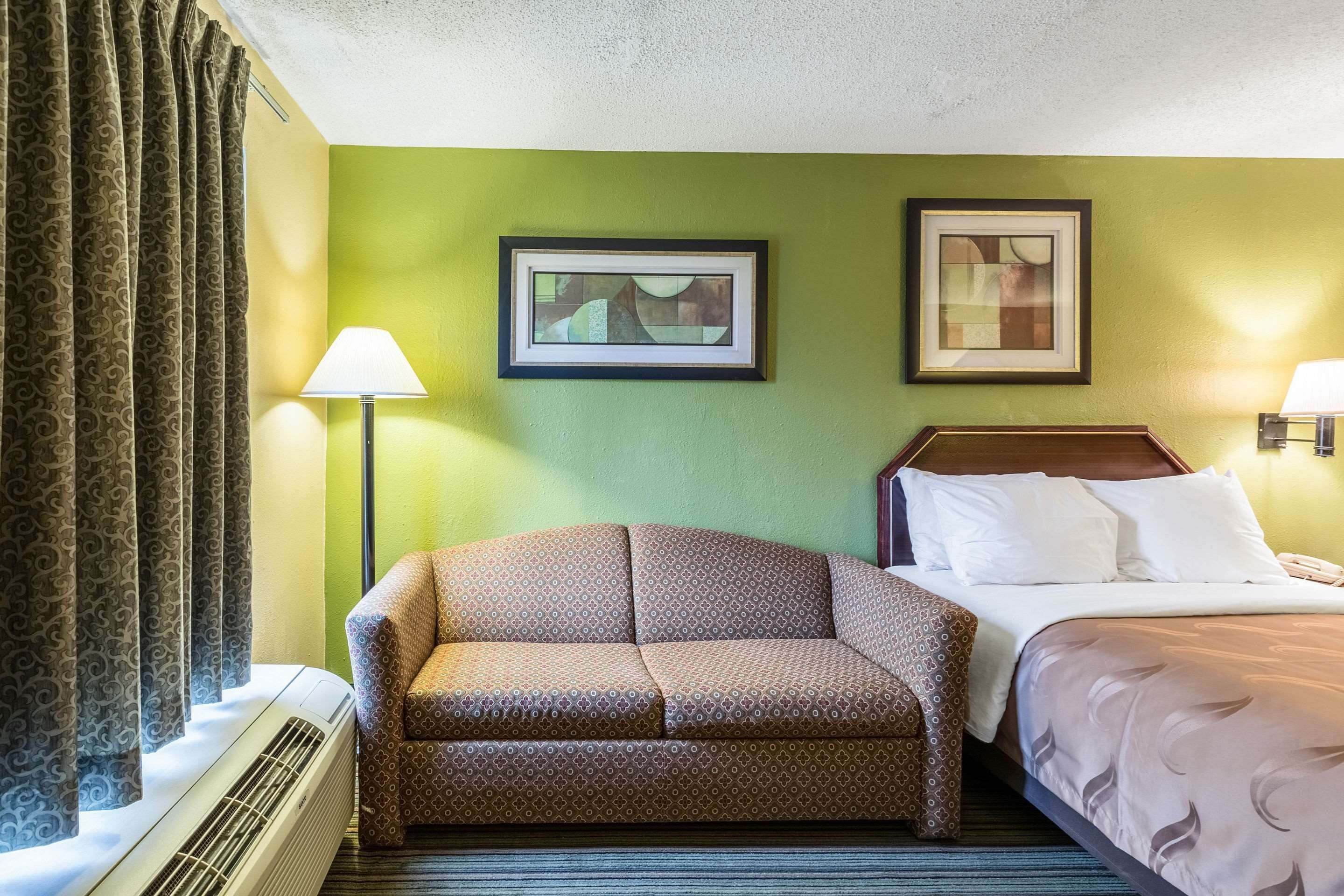 Une chambre d’hôtel avec un lit, un canapé, une lampe sur pied et un tableau encadré au mur.