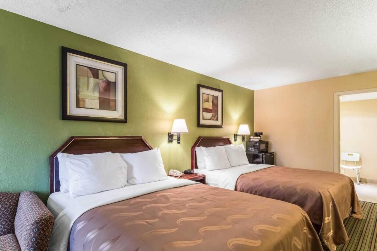 Ein Hotelzimmer mit zwei Betten, einem Schreibtisch, einem Stuhl und zwei gerahmten Bildern an der Wand.