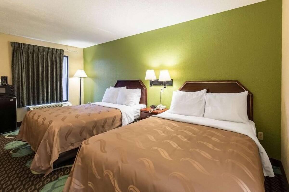Ein Hotelzimmer mit zwei Betten, einem Schreibtisch, einer Lampe und einem Fenster mit Vorhängen.