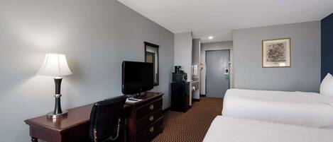 A hotel room with a desk, a television, a dresser, a bed, and a framed picture on the wall.