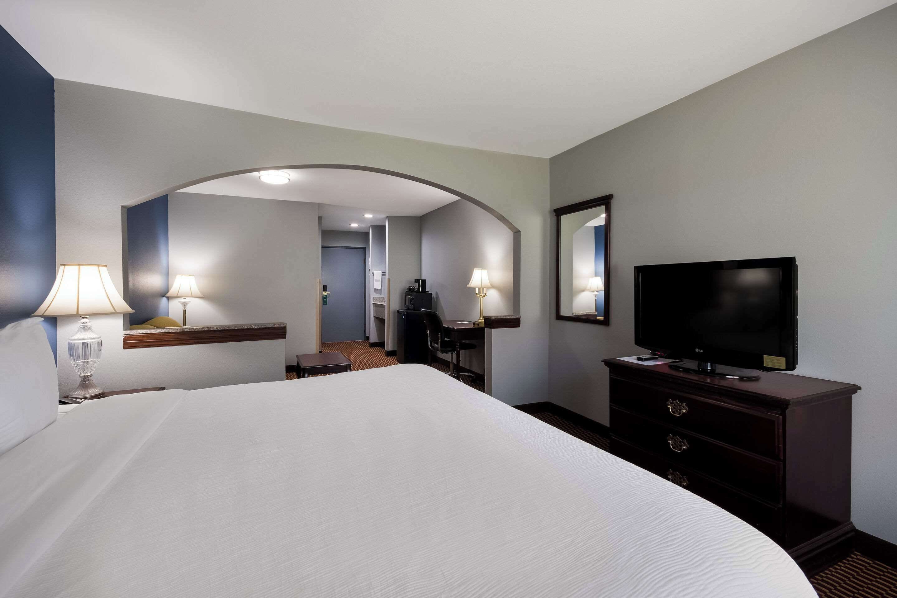 Habitación de hotel con una cama grande, un escritorio con silla, televisión y un espejo en la pared.