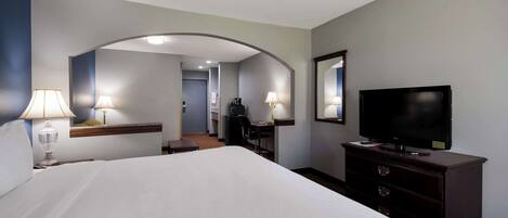 Habitación de hotel con una cama grande, un escritorio con silla, televisión y un espejo en la pared.