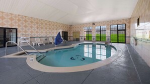 En inomhuspool med kaklade väggar, fri utsikt mot omgivningen och solstolar.
