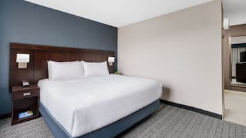 A hotel room with a large bed, a nightstand, a lamp, and a view of the hallway.