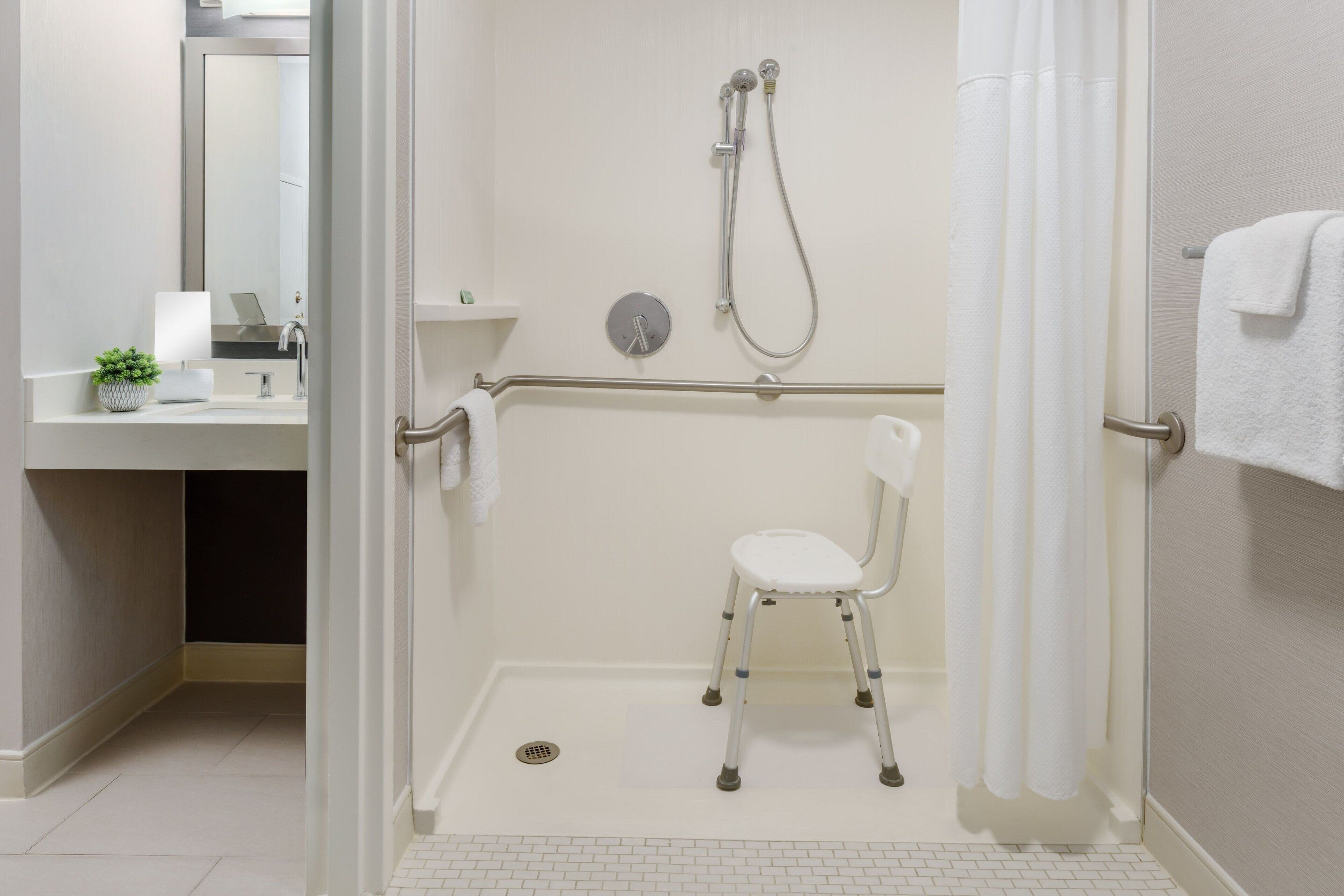 A bathroom with a shower, a toilet, a sink, and a chair.