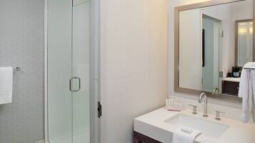 A modern bathroom with a glass shower enclosure, a white sink with a mirror above it, and a towel hanging on the wall.