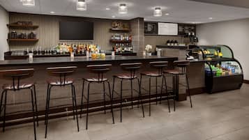 A bar area with a long counter, multiple stools, shelves with bottles, a TV, and a menu board.