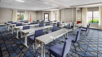 A conference room with multiple tables and chairs, a flag, and a view of greenery outside.