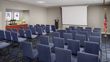 A conference room with rows of chairs, a podium, a projector screen, and an American flag.