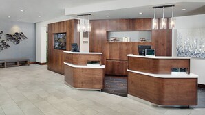 Zona de recepción con mostradores de madera, un banco y una pared decorativa con arte de vidrio.