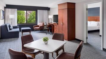 A hotel room with a bed, a desk, a TV, a sofa, and a dining area with chairs and a table.