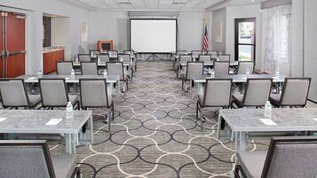 A conference room with rows of tables and chairs, a projector screen, and an American flag.