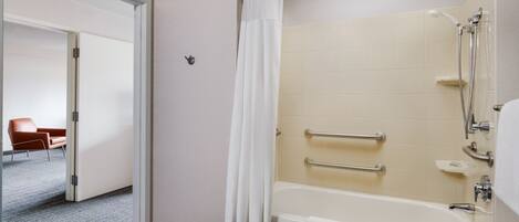 A modern bathroom with a bathtub, shower, and handrails.