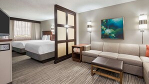 A hotel room with two beds, a sofa, a coffee table, a painting, and two wall lamps.