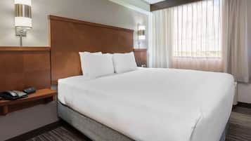 Habitación de hotel con una cama grande, cabecero de madera, mesita de noche con teléfono y ventana con cortinas.