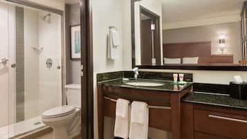Un baño de hotel con ducha de vidrio, un inodoro, un lavabo con espejo y un perchero para toallas.