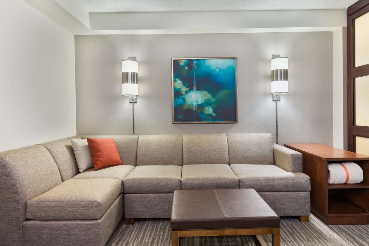 Une chambre d’hôtel moderne avec un canapé d’angle, une petite table en bois et un tableau au mur.