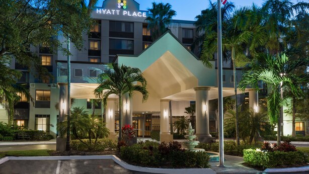 A Hyatt Place hotel with a modern design, featuring a prominent entrance, a flag, and lush landscaping.