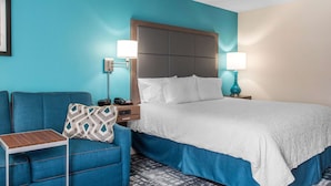 A hotel room with a large bed, a blue sofa, a small table, and two bedside lamps. - Hampton Inn Douglas (Douglas)