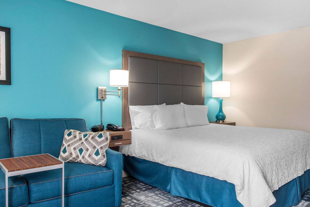 A hotel room with a large bed, a blue sofa, a small table, and two bedside lamps.